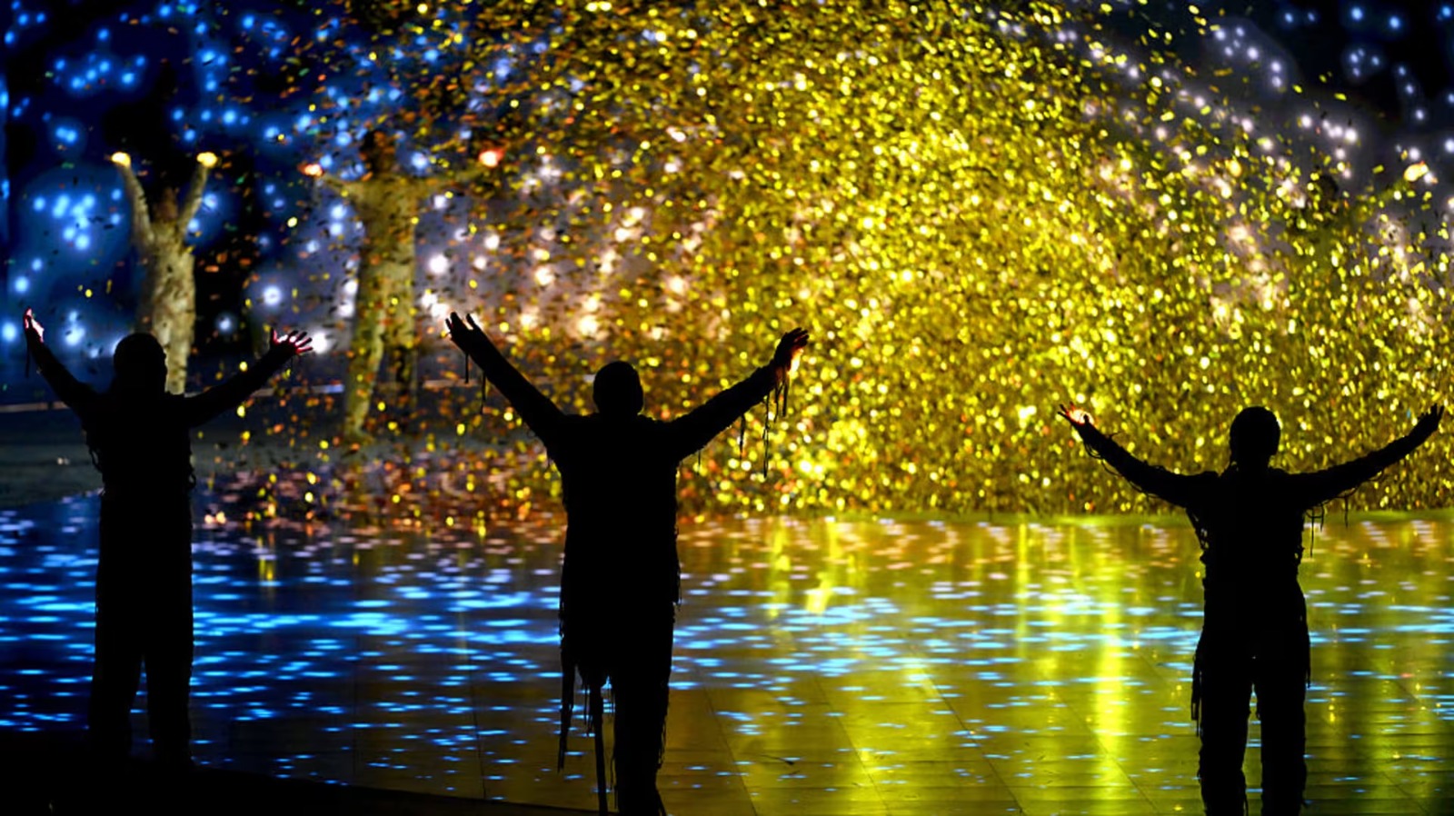 Tres ateltas de braços abertos diante de show de luzes