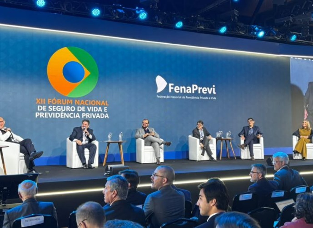 Imagem dos seis participantes do painel sentados em cadeiras  no palco do evento
