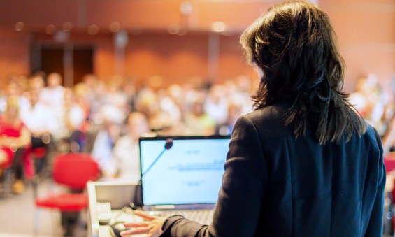 Mulher profere palestra para um auditório cheio de pessoas