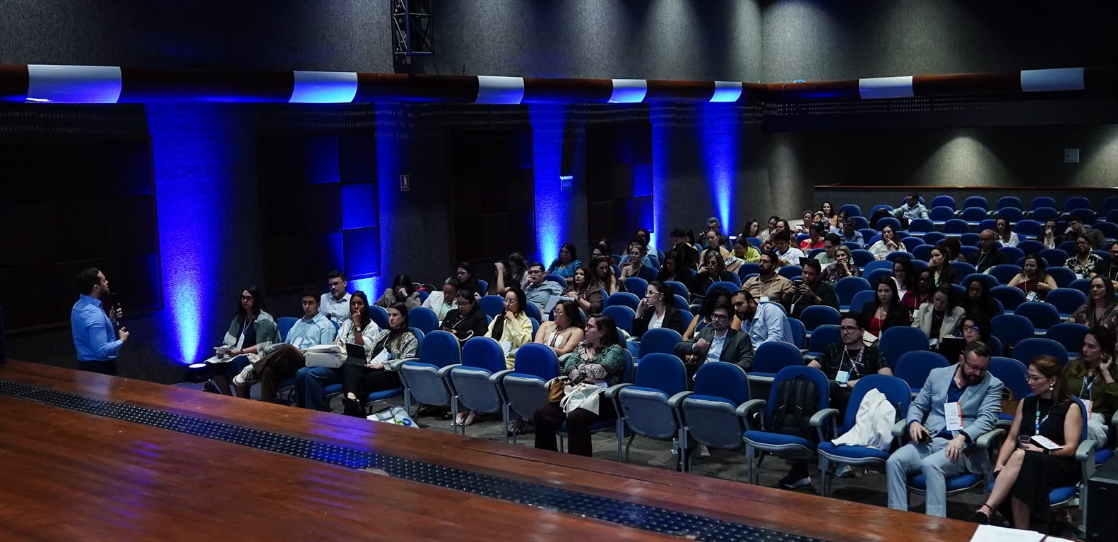 Pessoa falando ao microfone e pessoas sentadas