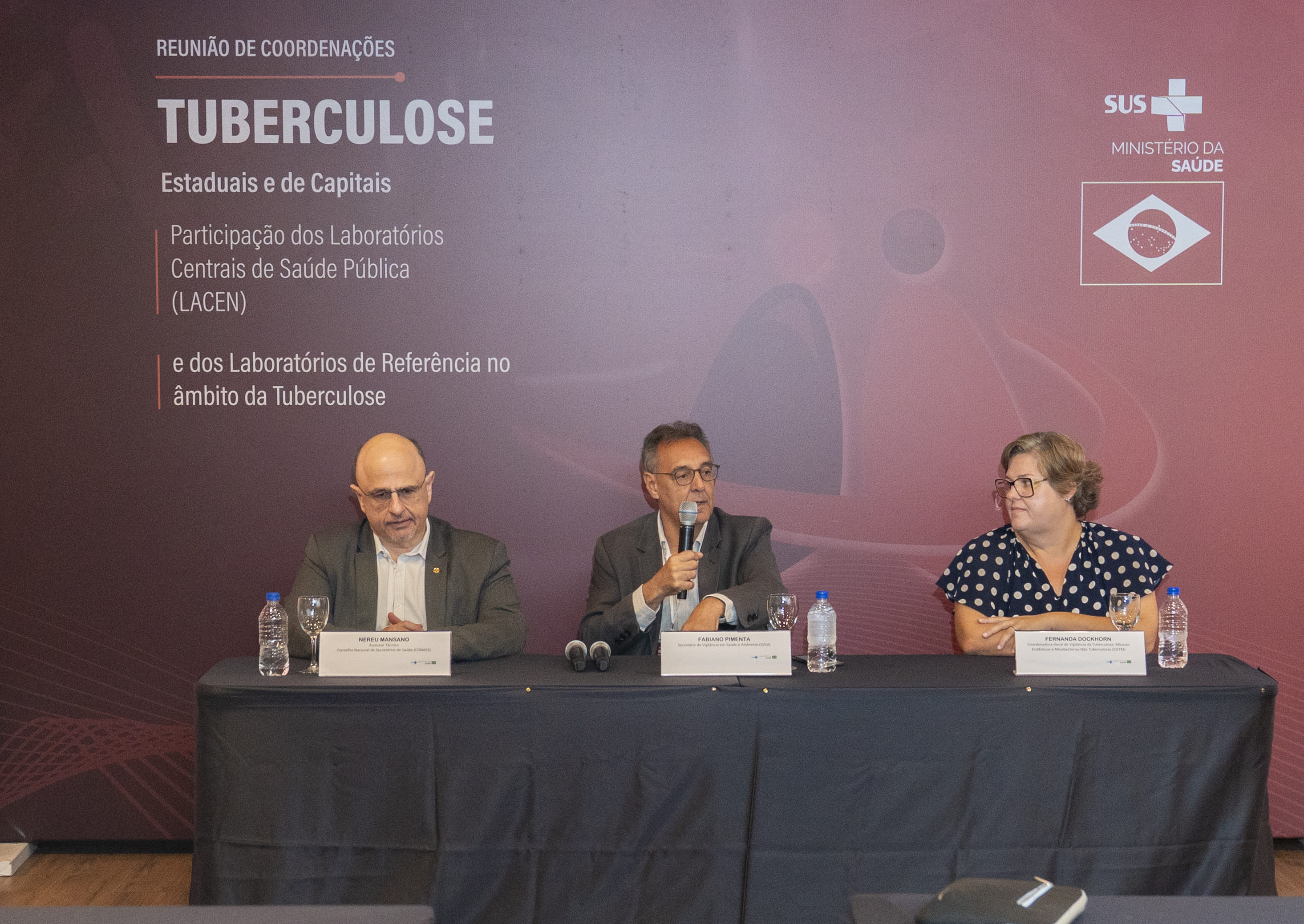 Pessoa falando ao microfone e pessoas sentadas