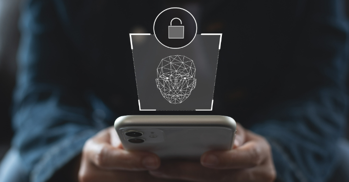 Pessoa segura um smartphone enquanto uma ilustração digital de reconhecimento facial e um cadeado aparece sobre a tela, representando a validação biométrica de identidade e a segurança no cadastro de usuários.