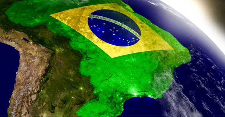 Imagem da Terra vista do espaço, com destaque para o território brasileiro coberto pela bandeira do Brasil.