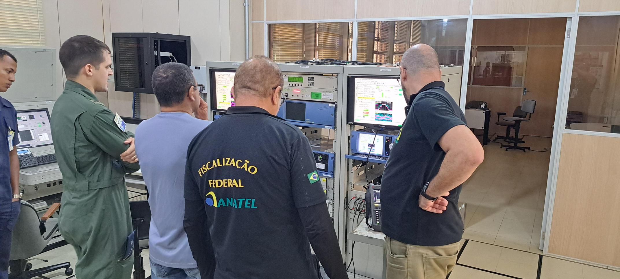Agentes da Anatel realizam ação de fiscalização em sala técnica.
