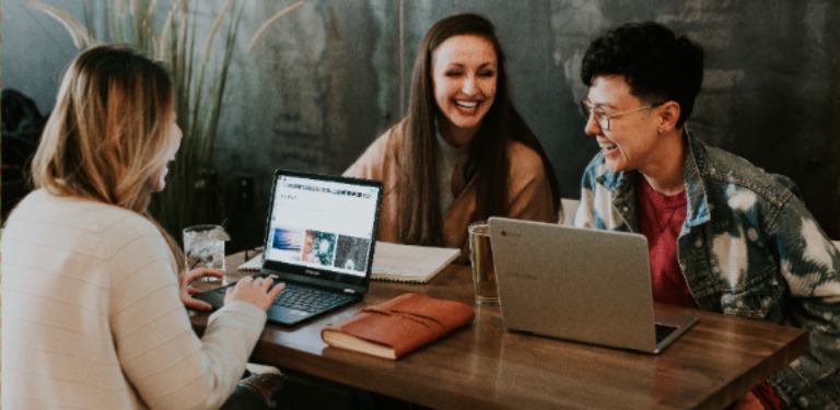 Três estudantes em uma mesa com notebooks e agenda