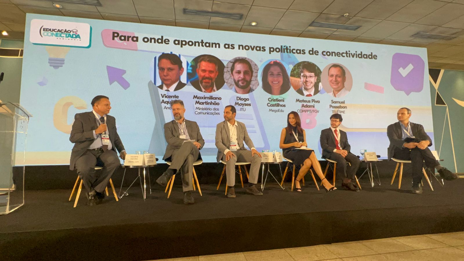 Participantes do Seminário Educação Conectada, entre os quais está o conselheiro da Anatel Vicente Aquino, estão sentados à frende de um painel onde se lê: “Para onde apontam as novas políticas de conectividade”.