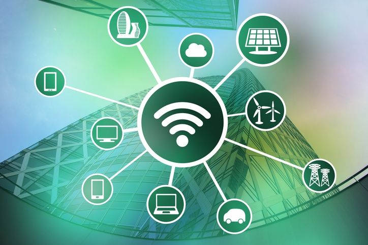 Ilustração de uma cidade moderna ao fundo, com um ícone central de Wi‑Fi conectado a símbolos de celular, computador, nuvem, painéis solares, turbinas eólicas, carro elétrico e infraestrutura urbana, representando conectividade e tecnologia inteligente.