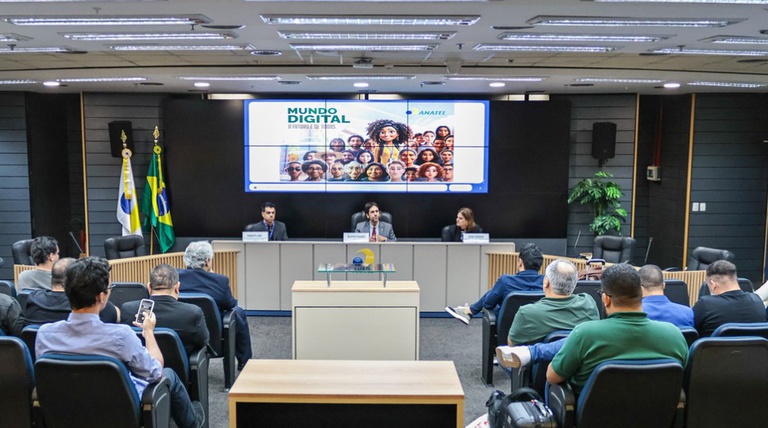 Foto mostra uma bancada com três pessoas em um auditório no qual estão sentados os participantes da primeira reunião ordinária dos Conselhos de Usuários das Prestadoras de Telecomunicações. de 2025