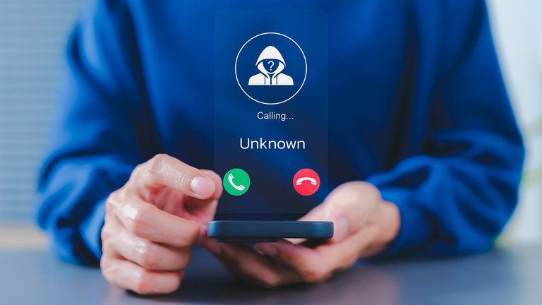 Uma pessoa em um moletom azul segura um smartphone que exibe uma chamada 'Desconhecida' com ícones de aceitar e recusar, flutuando como uma interface de usuário translúcida.
