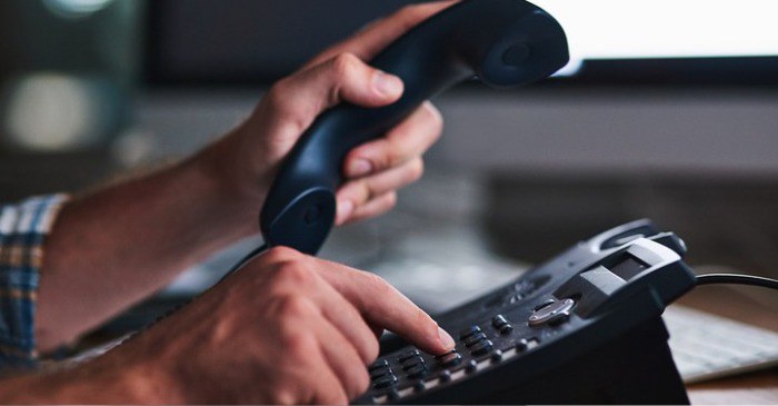 Mãos de uma pessoa fazendo uma chamada em um aparelho telefônico fixo