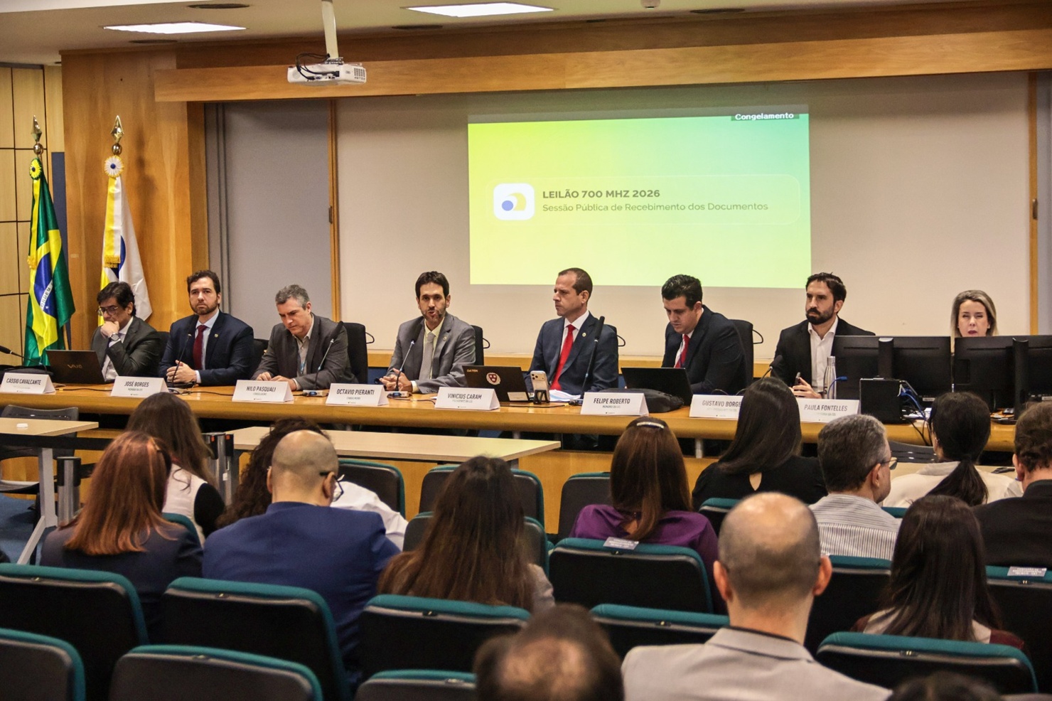 Servidores da Anatel sentados em bancada de auditório abrem a sessão de recebimento das propostas