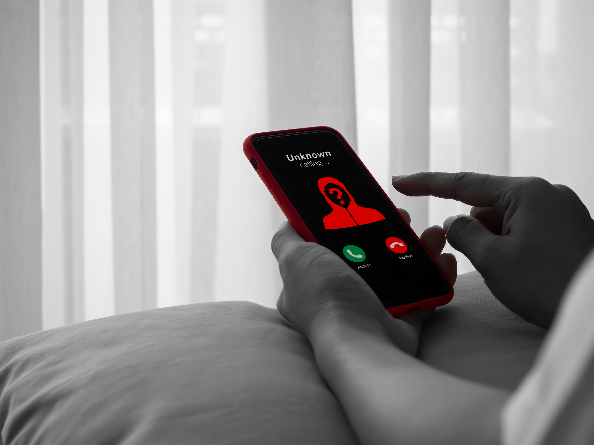 Conceito de alerta de chamada fraudulenta ou de golpista com número desconhecido aparecendo, figura encapuzada de vermelho na tela do smartphone, em uma foto em preto e branco. Phishing por telefone, cibercrime e risco de segurança móvel.