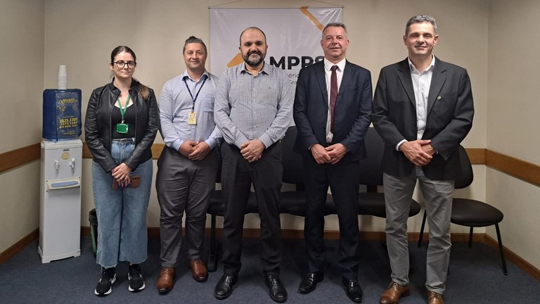 O gerente regional da Anatel no Rio Grande do Sul, Mauricio Peroni (segundo da direita, de terno), e sua equipe posam para uma foto em uma das reuniões institucionais em Pelotas. A comissão da Anatel encontra-se com representantes do Ministério Público Estadual ou do Procon de Pelotas. Ao fundo, um banner exibe o logotipo e nome parcial de uma das instituições, como 'MPP' ou 'Procon'