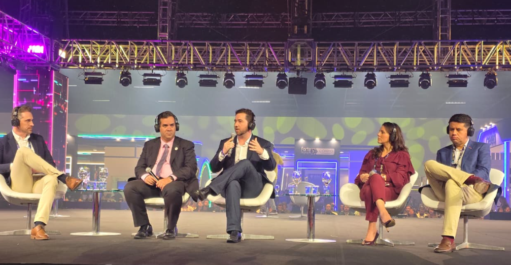 iMAGEM MOSTRA PESSOAS SENTADAS DEBATENDO EM UM PALCO
