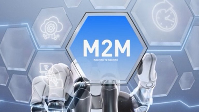 Uma mão robótica branca e cinza com detalhes azuis segura um hexágono azul translúcido com a inscrição "M2M MACHINE TO MACHINE" em branco. A mão e o hexágono estão sobrepostos a um fundo de outros hexágonos translúcidos interconectados, alguns contendo ícones brancos brilhantes de nuvem, engrenagens, rede e um relógio com uma seta. A iluminação é azul e futurista.