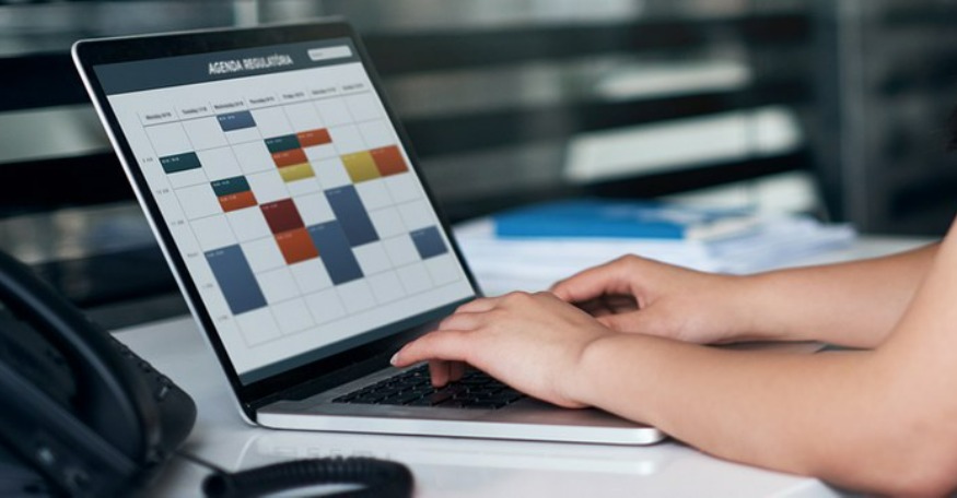 Mãos digitam em um laptop e na tela há um calendário em que está escrito Agenda Regulatória