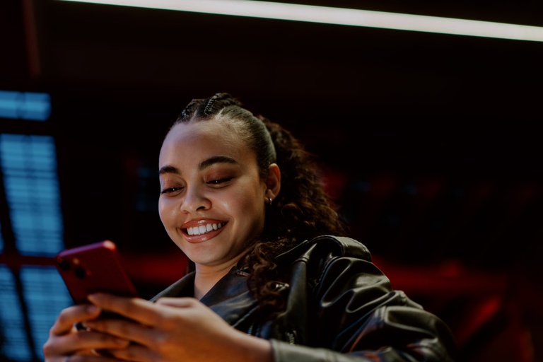 Imagem mostra mulher de aparência jovem, sorridente e de cabelos presos segurando um celular