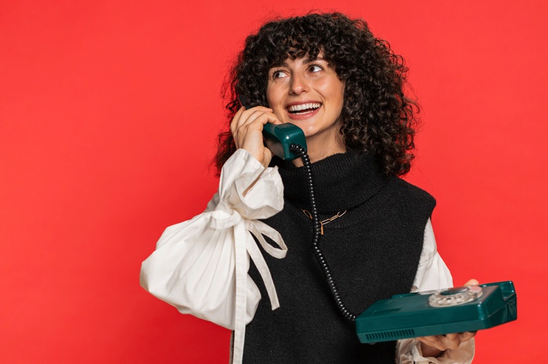 Imagem com fundo vermelho e uma mulher jovem segurando um telefone fixo verde