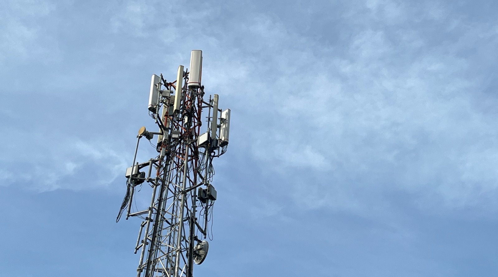 Torre de telefonia celular e transmissão sob céu azul.