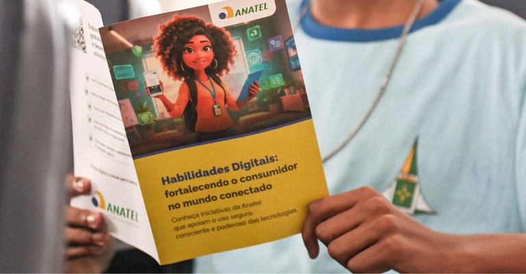 Jovem segurando um folheto da Anatel com ilustração de personagem digital usando celular e o título “Habilidades Digitais: fortalecendo o consumidor no mundo conectado”.