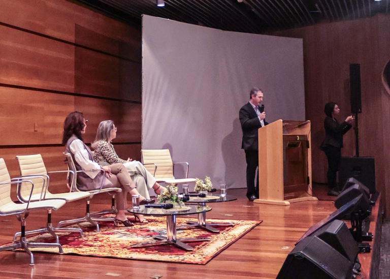 Imagem do auditório do Espaço Cultural da Anatel com três pessoas no palco