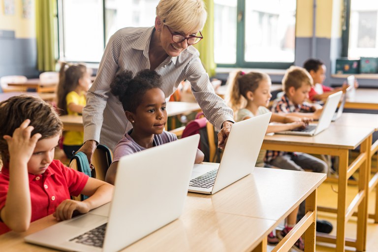 Crianças e professora utilizando laptops em sala de aula
