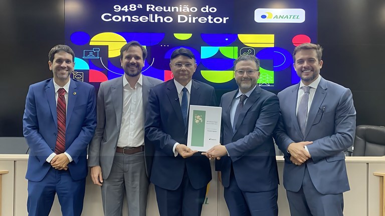Uma fotografia mostra cinco homens de terno posando em uma sala de conferências. Da esquerda para a direita, eles são: o conselheiro Octavio Pieranti, o presidente Carlos Baigorri, e os conselheiros Vicente Aquino, Alexandre Freire e Edson Holanda. Ao fundo, um grande pôster branco exibe o logotipo da ANATEL e o texto "948ª Reunião do Conselho Diretor"
