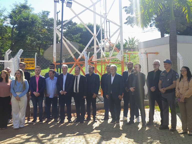 Grupo de pessoas enfileirado lado a lado em frente a uma antena de TV