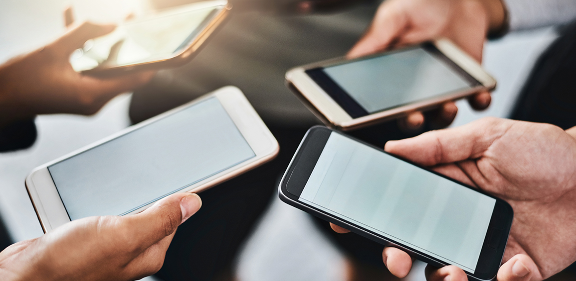 A imagem apresenta quatro pessoas em círculo e ao centro são visíveis os celulares, suas telas e as mãos que os seguram