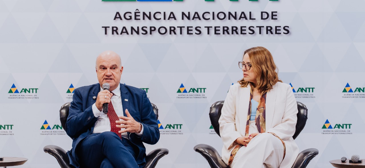 IMAGEM COM UM HOMEM E UMA MULHER SENTADOS NO PALCO DO AUDITORIO DA ANTT
