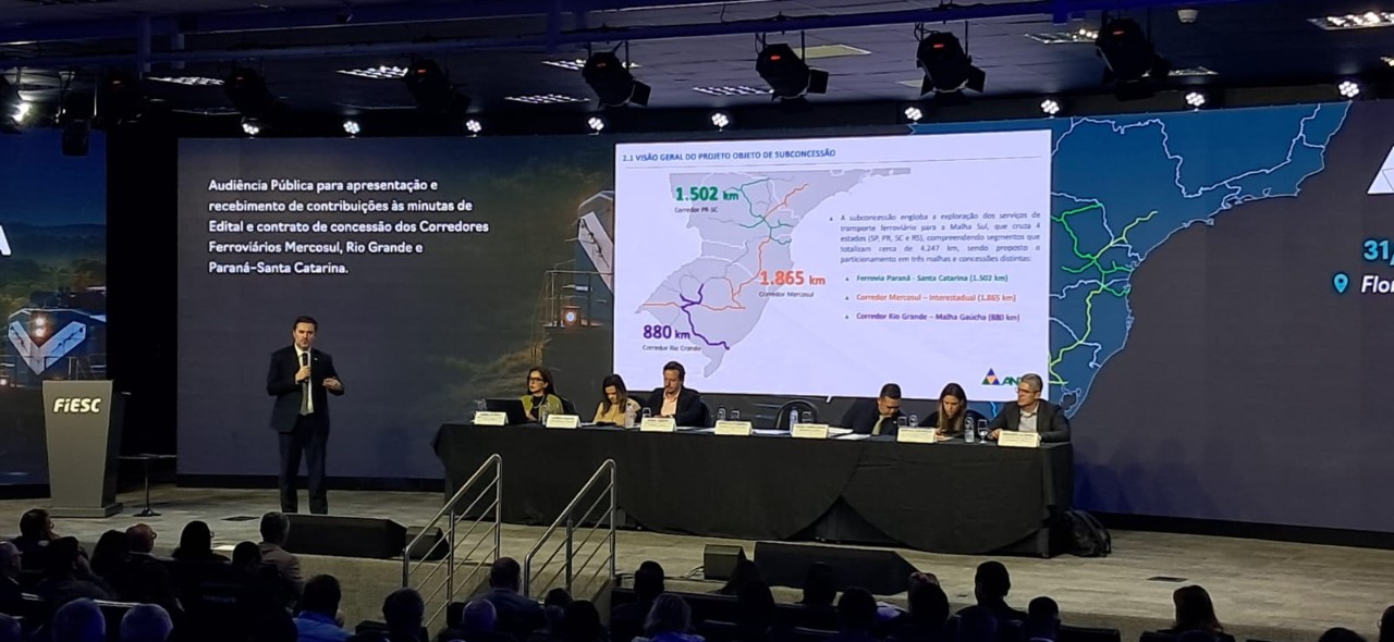IMAGEM DA AUDIENCIA PUBLICA, COM O PUBLICO SENTANDO, SEIS PESSOAS SENTADAS E UMA EM PÉ EM FRENTE AO PAINEL