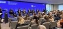 SETE PESSOAS SENTADOS EM CADEIRAS COM UM PUBLICO ASSISTINDO