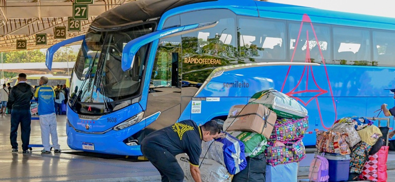 IMAGEM DO ONIBUS COM PESSOAS NA FRENTE CARREGANDO BOLSAS