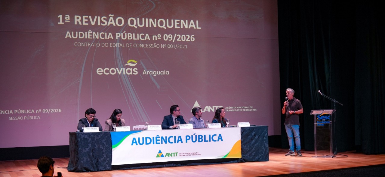 IMAGEM DO AUDITORIO COM 5 PESSOS ATRAS DA MESA