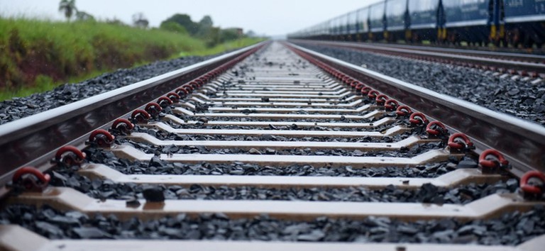 Foto mostrando os trilhos de uma ferrovia e o trem passando ao lado