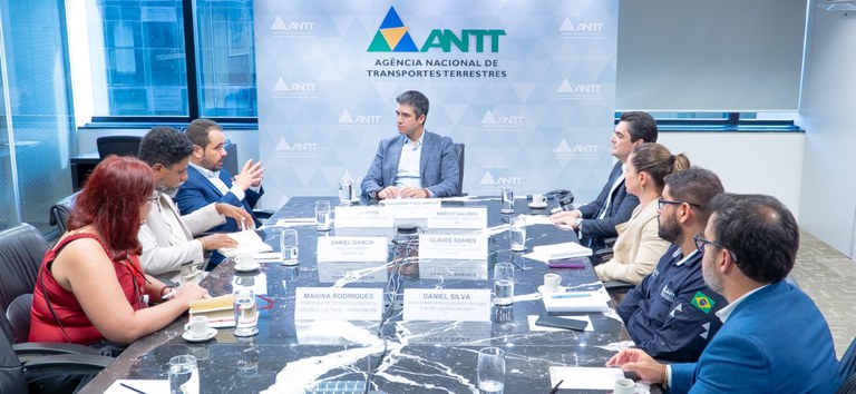 Foto com diretor da ANTT, presidente da Sinagências e demais representantes sentados à mesa na reunião