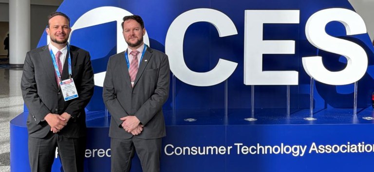 Foto mostrando o diretor e o coordenador da ANTT em frente ao banner do CES 2026