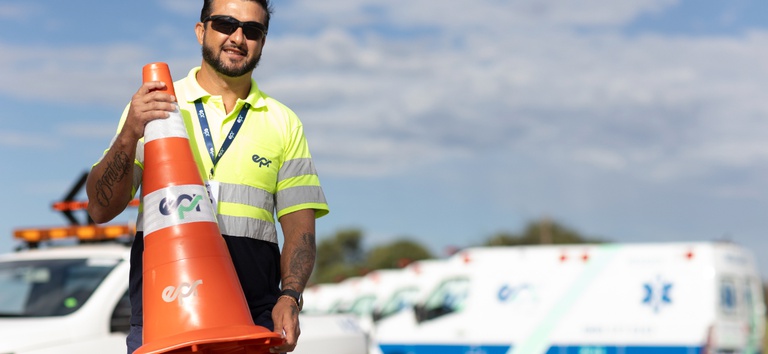 Foto mostrando funcionário com cone na mão e estrutura de veículos da concessão atrás
