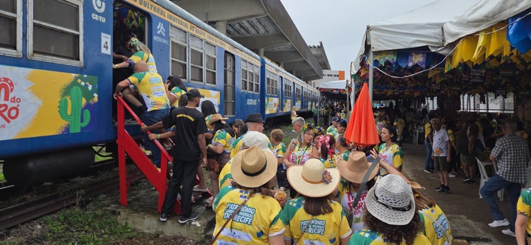 IMAGEM COM PESSOAS ENTRANDO NO TREM, COM CHAPEUS E BLUSAS FESTIVAS