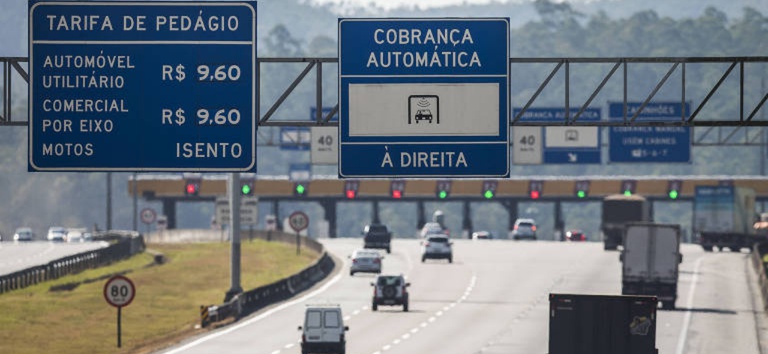 Foto mostrando rodovia com placa de pedágio e pedágio a frente