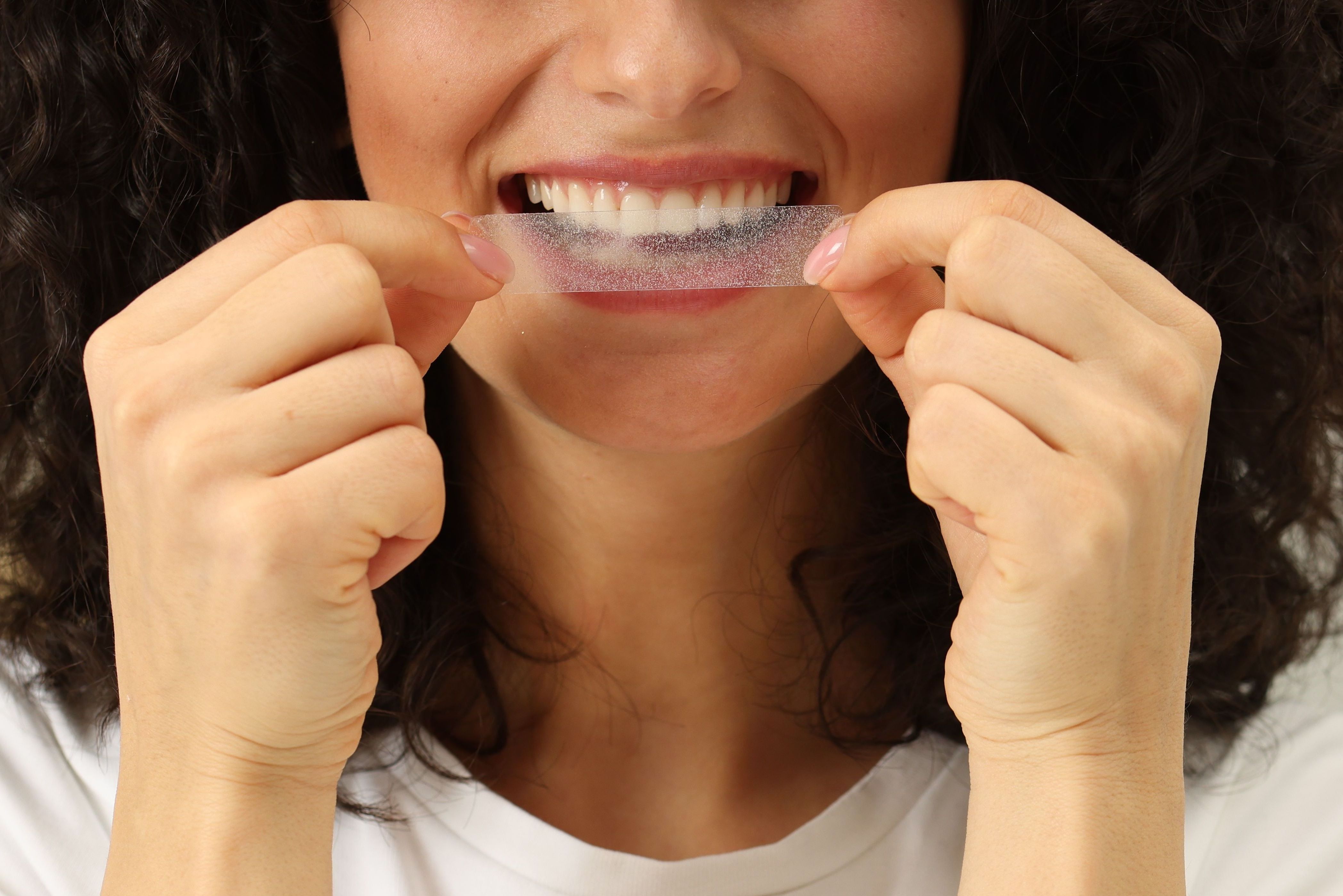 mulher segura fita clareadora próxima aos dentes