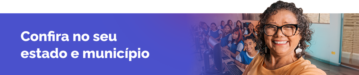 Professora está em pé e sorri tirando foto com alunos sorrindo e sentados ao fundo numa sala de aula..