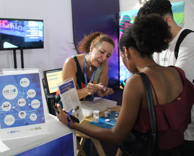 Mônica Ramalho, servidora do CBPF e colaboradora NIT Rio, apresentando a hidroxiapatita aos visitantes.Crédito: Tatiana Azzi