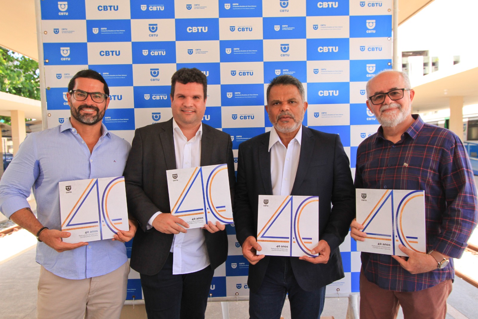 diretor-presidente José Marques, Superintendente de Maceió Carlos Jorge e empregados da CBTU reunidos segurando o livro de 40 anos da empresa