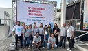 Grupo de pessoas em pé na frente de um banner branco com a frase Conferencia Nacional das Cidades