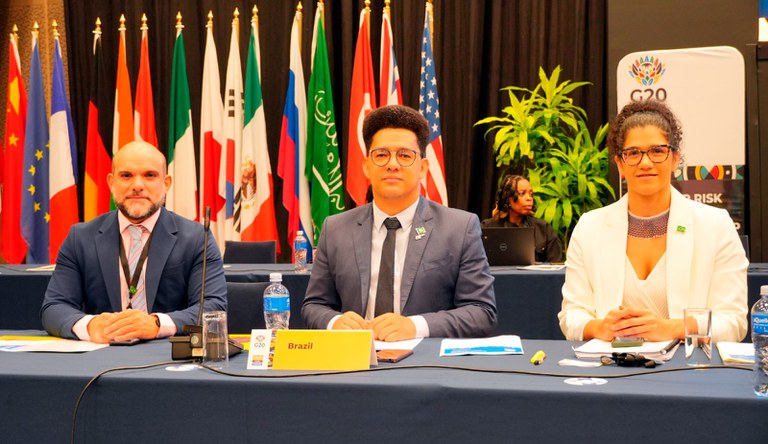 Dois homens sentados, com blazer azul marinho e uma mulher negra, cabelos cacheados com blazer branco.