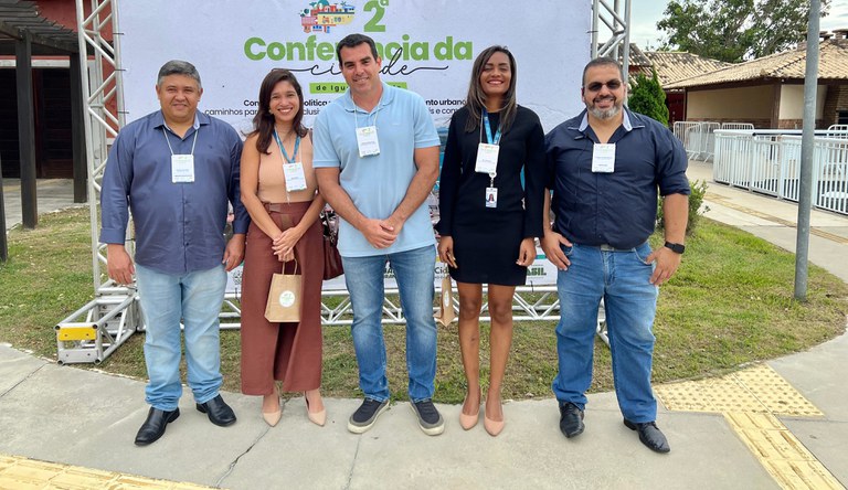 Imagem de cinco pessoas posando na frente de um painel