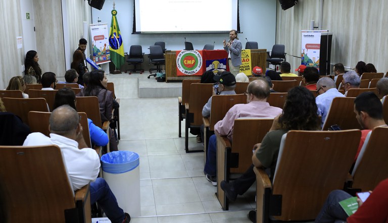 Na foto palestrante fala ao público sentado a sua frente.