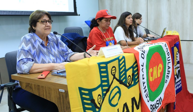 Na foto há 4 pessoas sentadas numa mesa, uma delas com boné vermelho.