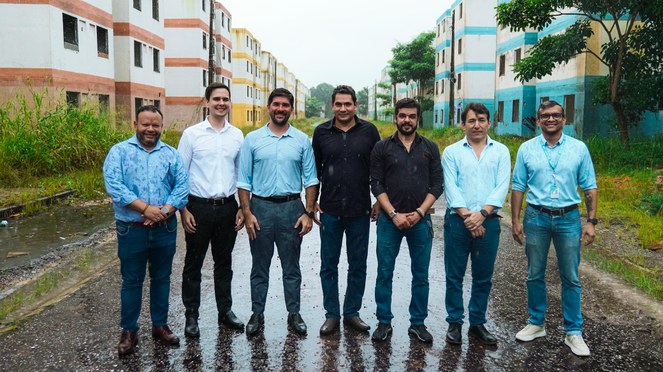 Na foto a equipe do ministério das Cidades, de sete pessoas, posam na chuva no condomíno do MCMV